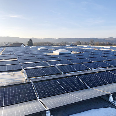 Ein Firmendach mit Photovoltaik-Anlagen bedeckt, im Hintergrund Landschaft mit Himmel